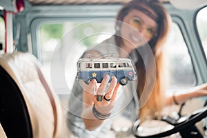 Young hippie woman driving a classic van with a toy car model in her hand. Smiling blurred girl holding a miniature