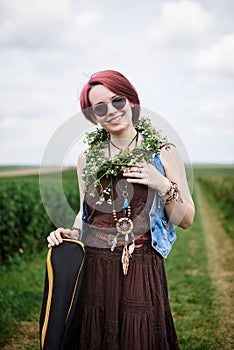 Young hippie woman with short red hair, wearing boho style clothes, sunglasses, with flower wreath on neck, standing on green