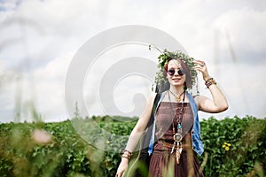 Young hippie woman with short red hair, wearing boho style clothes, sunglasses and flower wreath, standing on green field, holding