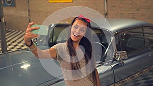 Young Hipser Pin-up Mixed Race Girl Taking Selfie with Mobile Phone at Vintage Garage and Old Car. 4K, Slowmotion.