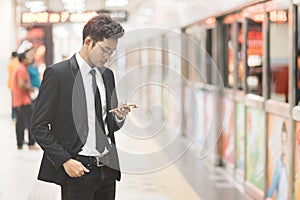 Young hipster asian businessman using smartphone while waiting for a train in subway. Concept of wireless technology, mobile