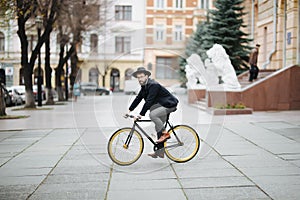 Young hipster bearded man riding bicycle to work on urban street