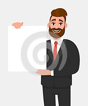 Young hipster business man showing blank white poster or paper copy space area. Happy trendy person holding empty banner.