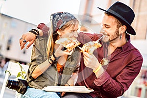 Young hipster couple eating pizza at bar restaurant outdoors - Happy relationship concept with millenial boyfriend and girlfriend