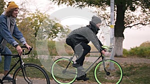 Young hipster couple enjoying cycling through park on trekking bikes. Two young people having great time together in