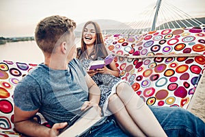 Young hipster couple reading books in a hammock at the beach at sunset, freelancer leisure man and woman  on a beach trip, summer