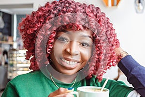 Young hipster dark-skinned woman dressed in casual clothes holding cup of hot drink, enjoying coffee or tea