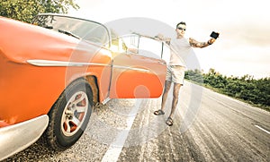 Young hipster fashion man with tattoo taking selfie with vintage car during road trip in Cuba - Travel wanderlust concept photo