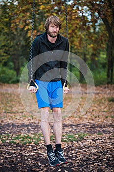 Young hipster fit man pulling up on gymnastic rings outdoors