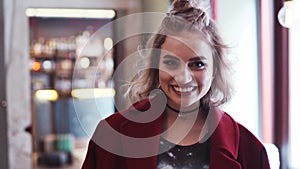 Young hipster girl with casual outfit looks right in the camera and smiles happily. Stylish look, red coat, light makeup