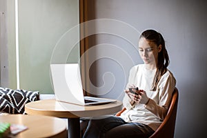 Young hipster girl chatting on mobile phone while resting with laptop computer in coffee shop.