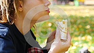 Young hipster girl with dreadlocks eats kebab. Girl eats fast food shawarma in the park. Sunny day.