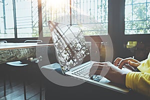 Young hipster girl hands working on her laptop sitting at wooden table in a coffee shop.