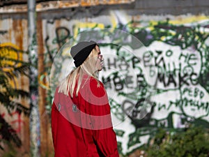 Young hipster girl in a knitted hat goes on the background of a wall with graffiti