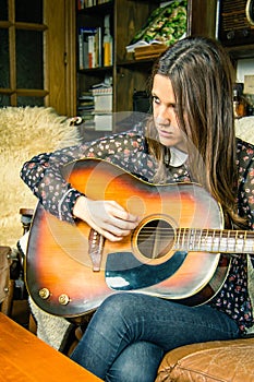 Young hipster girl playing acoustic guitar at home