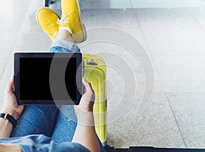 Young hipster girl sitting at airport and put feet in yellow boot on suitcase traveling in Europe, female hands texting message on