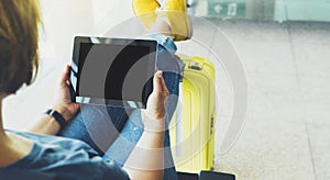 Young hipster girl sitting at airport in yellow boot on suitcase traveling in Europe, female hands using app on making tablet