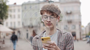 Young hipster guy with glasses chatting with friends at social networks and listen music, using modern smartphone device