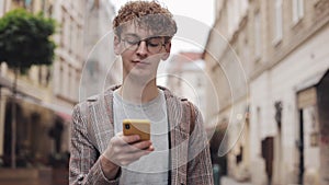 Young hipster guy with glasses chatting with friends at social networks and listen music, using modern smartphone device