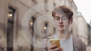 Young hipster guy with glasses chatting with friends at social networks and listen music, using modern smartphone device