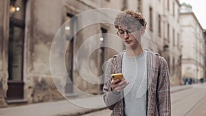 Young hipster guy with glasses chatting with friends at social networks and listen music, using modern smartphone device