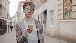 Young hipster guy with glasses chatting with friends at social networks and listen music, using modern smartphone device