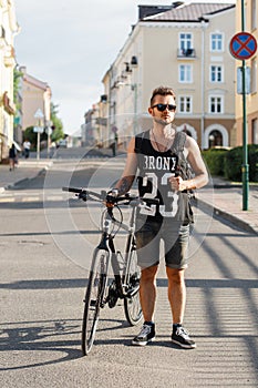 Young hipster man with bicycle walking in the city. Black T-shirt with print 23