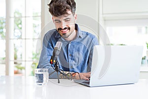 Young hipster man recording podcast using laptop, broadcasting an interview using microphone