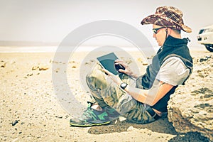 Young hipster man sitting in desert road - Technology concept