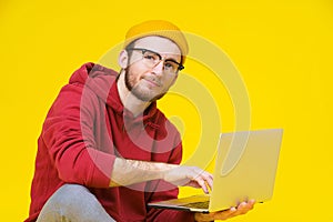 Young hipster man sitting on the floor holding laptop in red hoodie studying or working. Smart freelancer caucasian man