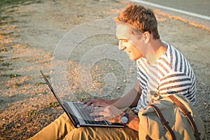 Young hipster man sitting outdoors checking mails on laptop