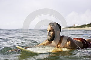 Young hipster man swimming on the surfboard into the sea water waiting for a big wave - Cool guy having fun doing extreme sport -