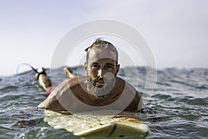 Young hipster man swimming on the surfboard into the sea water waiting for a big wave - Cool guy having fun doing extreme sport -