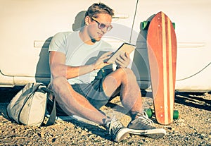 Young hipster man with tablet sitting next his car
