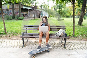 Young hipster millennial freelance woman with cool attitude, expatriate exchange student, sitting in park working online on laptop photo