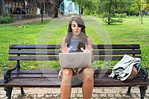 Young hipster millennial freelance woman with cool attitude, expatriate exchange student, sitting in park working online on laptop photo