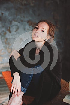 Young hipster redhead woman relaxing at home, sitting on wooden table with books