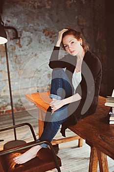 Young hipster redhead woman relaxing at home, sitting on wooden table with books