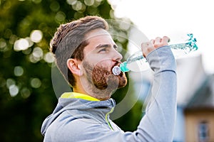 Young hipster runner in town with water bottle, drinking