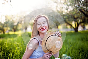 Young hipster stylish woman laughs and holds a straw hat, red lips, blue sarafan. Happy girl rejoices in the summer, the sun and s