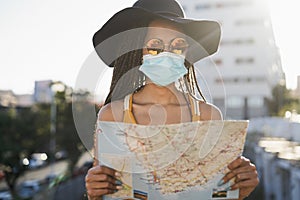 Young hipster tourist girl using map outdoor while wearing safety mask on travel vacation - Focus on face