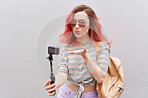 Young hipster woman with coloured pink hairs making vlog by action camera. Kissing