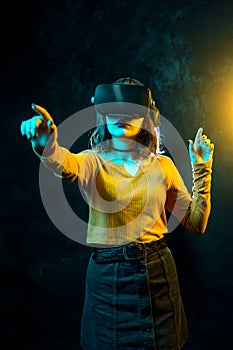 Young hipster woman with curly hair wearing virtual reality goggles and touch another world in studio neon lights