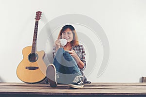 Young hipster woman drinking coffee chillin` with guitar sittin