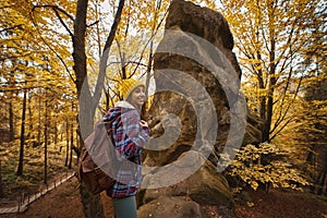 Young hipster woman enjoying walk in autumn golden forest with mossy boulders in Carpathian