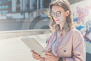 Young hipster woman in glasses stands on city street and uses tablet computer.Girl looking on screen of digital tablet.