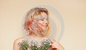 Young hipster woman with pink colored flying curly hairs and wildflowers smiling