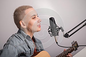 Young hipster woman is recording a song at home recording studio. The girl plays an acoustic guitar and sings into a