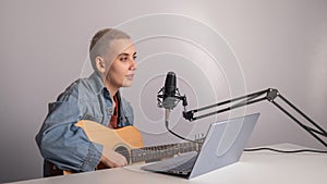 Young hipster woman is recording a song at home recording studio. A girl plays an acoustic guitar sings into a