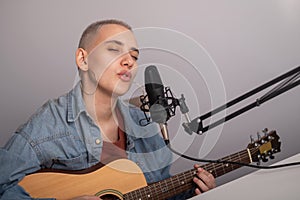 Young hipster woman is recording a song at home recording studio. The girl plays an acoustic guitar and sings into a
